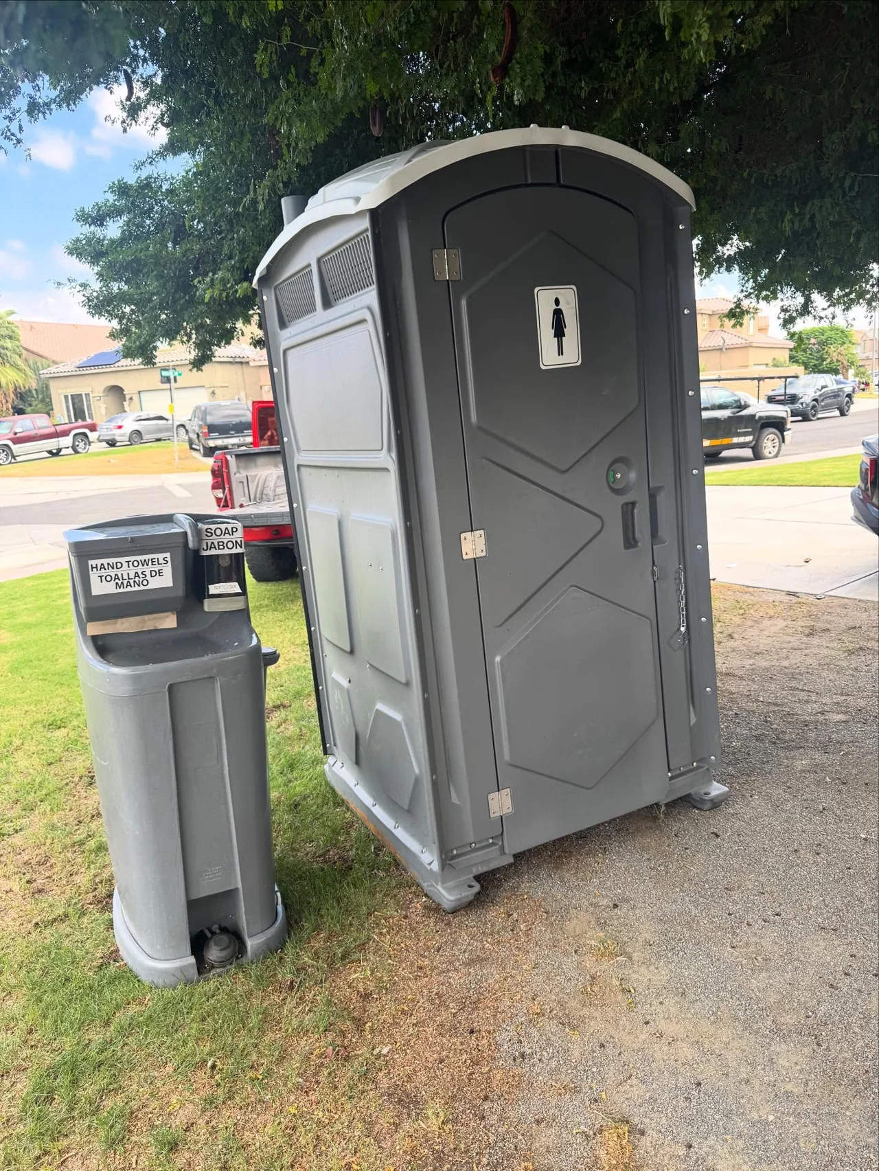 Gray portable restroom and an exterior handwash station in an outdoor setting
