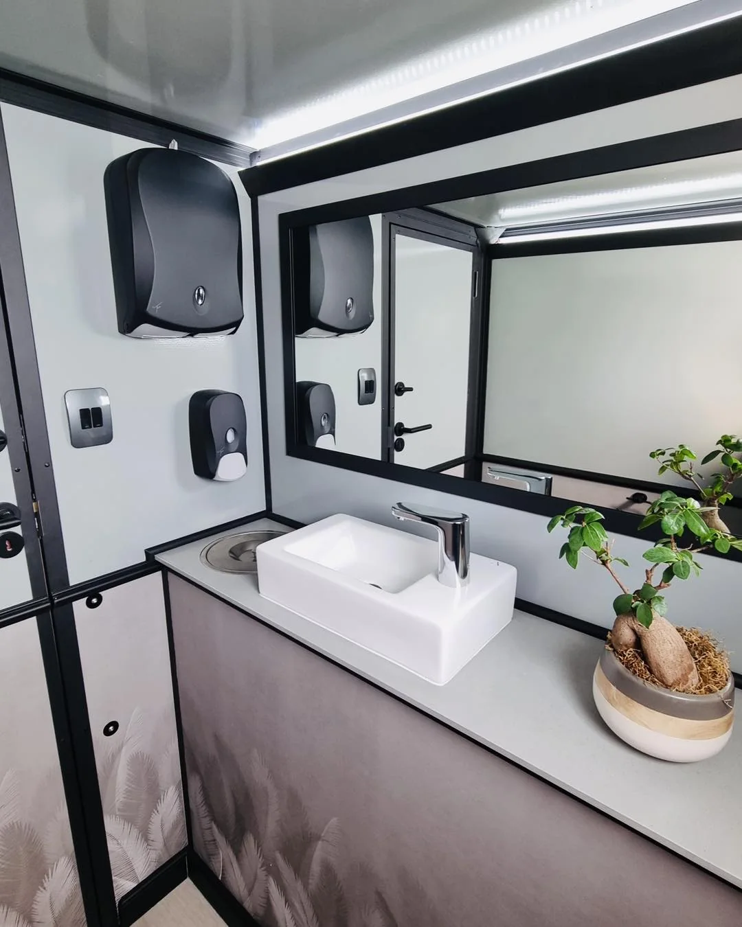 Restroom trailer vanity with mirror, sink, and lighting